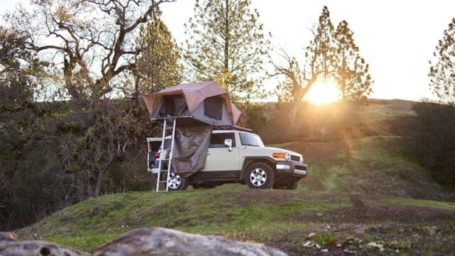 An FJ cruiser off-roading with a rooftop tent affixed to its roof rails.
