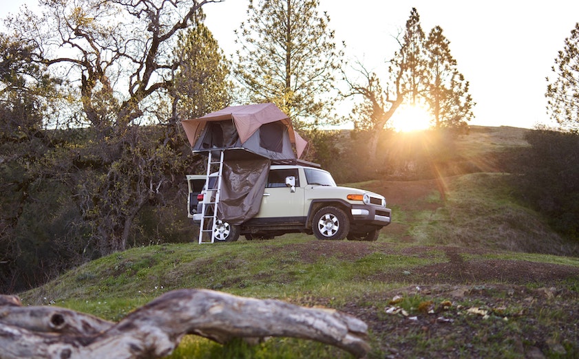 An FJ cruiser off-roading with truck accessories including a rooftop tent affixed to its roof rails.